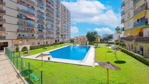 A large swimming pool surrounded by a well-maintained lawn, with multi-story buildings in the background.