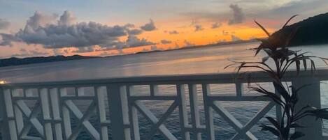 A deck with a railing overlooking a calm body of water during sunset.