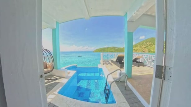 An outdoor swimming pool with a view of the sea and a small boat in the distance.