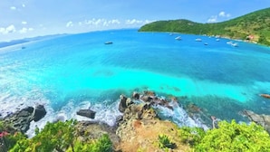 A coastal view with clear turquoise waters, rocky shoreline, and boats.