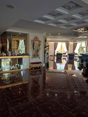 A luxurious lobby with a marble floor, ornate ceiling, and a reception area with a large mirror and decorative items.