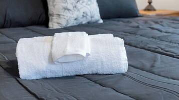 Un lit bien fait, avec une serviette blanche roulée, une literie sombre et une lampe sur une table de chevet.