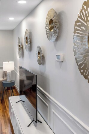 Un salon moderne avec un téléviseur à écran plat, des œuvres d’art décoratives au mur, une lampe et une table d’appoint.