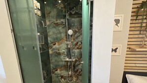 A modern bathroom with a glass-enclosed shower, marble walls, and a wooden floor. -  High Speed WiFi City Centre Flat (Thessaloniki)