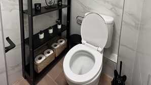 A modern bathroom with a toilet, a black shelf unit with decorative items, and a window. -  High Speed WiFi City Centre Flat (Thessaloniki)
