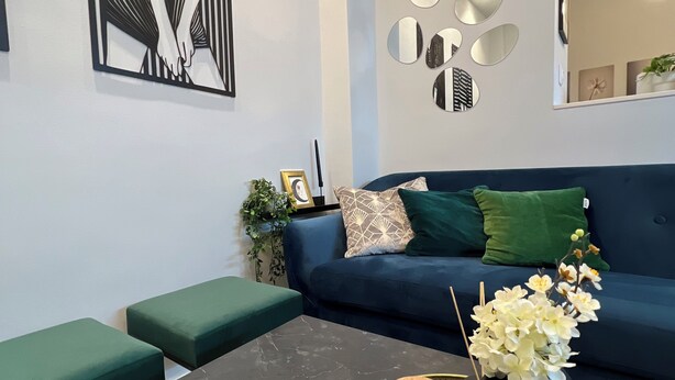 A modern living room with a dark sofa, green cushions, a coffee table with decorative items, and a wall art piece. -  High Speed WiFi City Centre Flat (Thessaloniki)