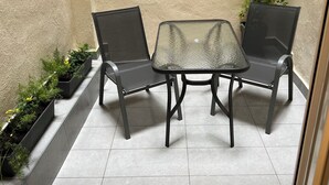 A small patio with a glass table and two chairs, surrounded by potted plants and a textured wall. -  High Speed WiFi City Centre Flat (Thessaloniki)
