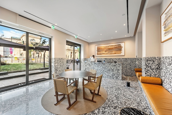 A modern interior with a round table and chairs, a bench, and a large window offering a view of the street.