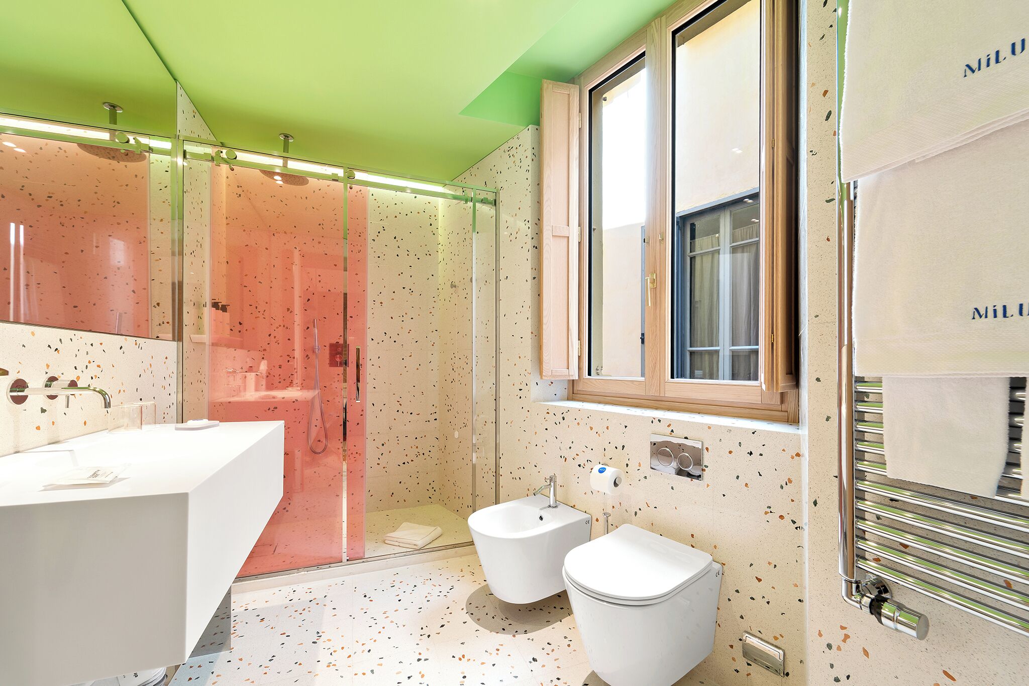 Un bagno moderno con un lavandino bianco, due bidet, una cabina doccia in vetro e un porta asciugamani.
