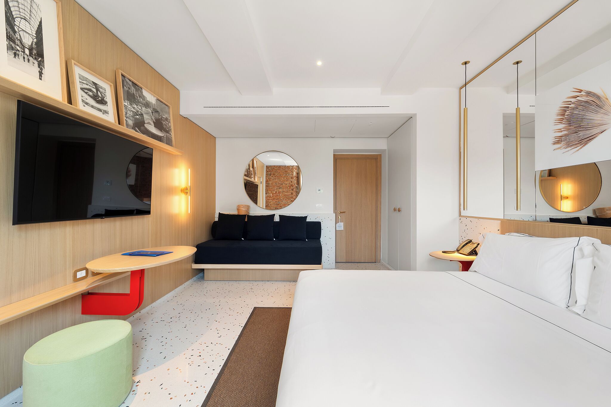 A modern hotel room with a bed, a sofa, a TV, and a mirror.
