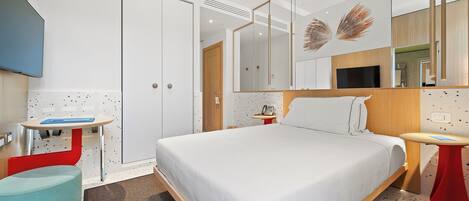 A modern hotel room with a large bed, a bedside table, a small desk, a chair, and a large mirror.