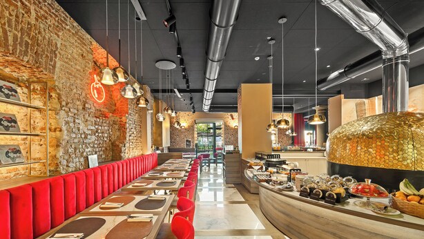 A modern restaurant with a long counter, red cushioned seating, and a variety of food items displayed. - Hotel Milu Milano (Milan)