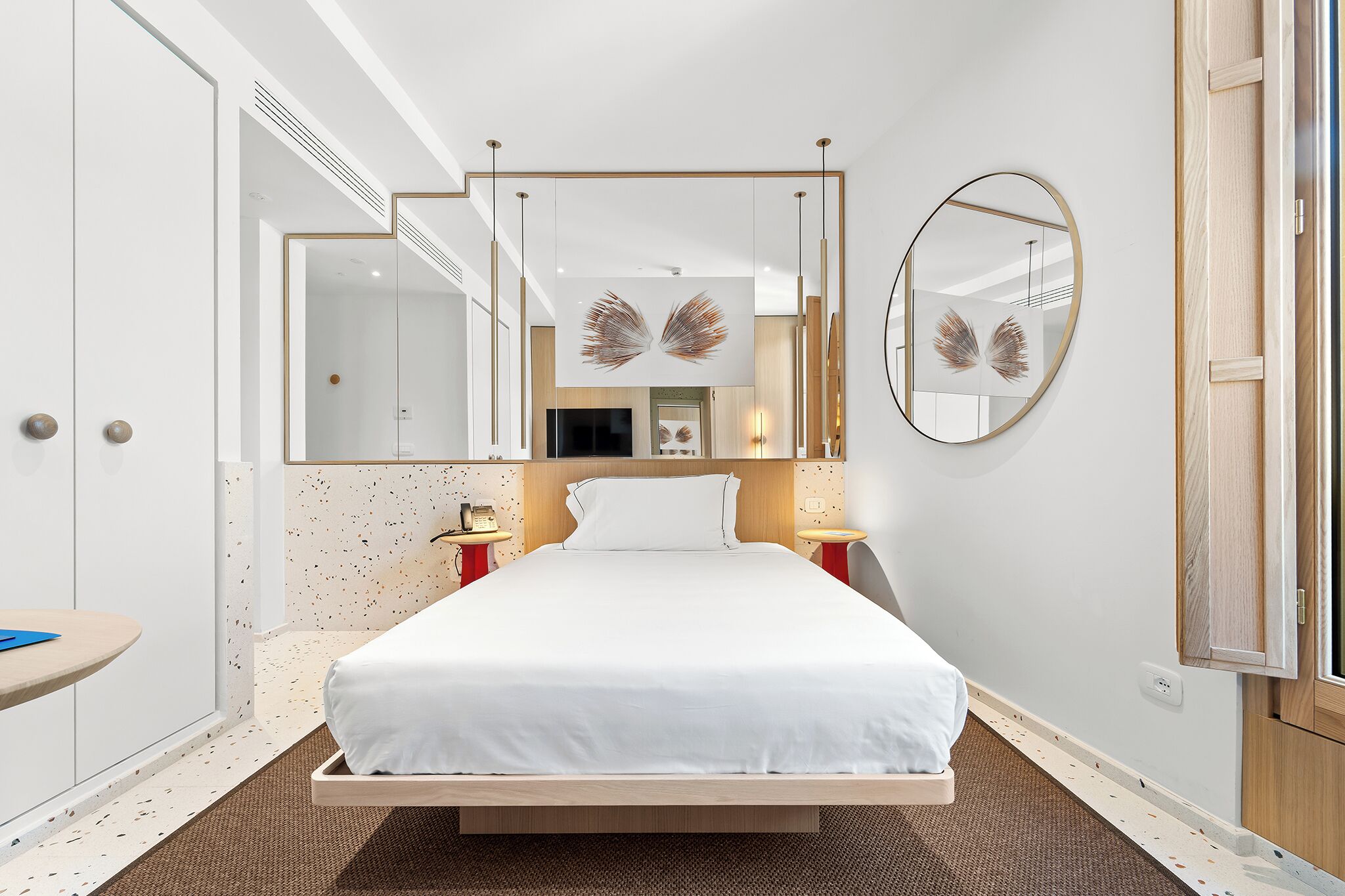 A modern hotel room with a large bed, a round mirror, and a small bedside table.