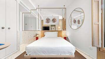 A modern hotel room with a large bed, a round mirror, and a small bedside table.