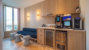 A modern kitchenette with a built-in coffee machine, a mini-fridge, and a water dispenser. There is a blue sofa and patterned stools in the seating area. - Hotel Milu Milano (Milan)