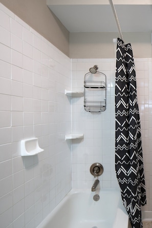 Un bagno con pareti piastrellate di bianco, una doccia con tenda a righe bianche e nere, e un porta asciugamani.