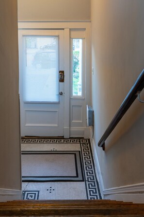 A staircase leading to a door with a patterned rug and a window with blinds.