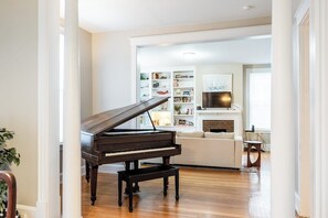 A grand piano in a spacious living room with a fireplace, bookshelves, and a cozy seating area.