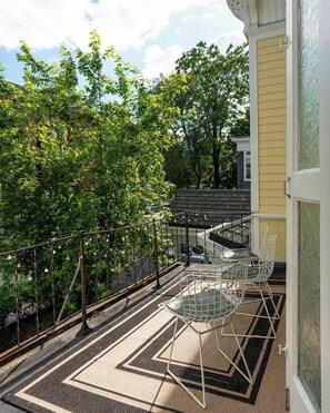 A balcony with a patterned rug, a metal chair, and a view of trees and a building.