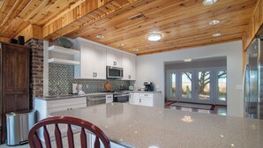 A modern kitchen with a large island, white cabinetry, a herringbone tile backsplash, and a wooden ceiling. - Cypress Chaos beautiful home with incredible marsh views in Willowbank (Georgetown)