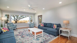 A living room with a blue sofa, a white coffee table, and a patterned rug. - Cypress Chaos beautiful home with incredible marsh views in Willowbank (Georgetown)