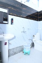 Un baño con un lavamanos blanco, un espejo, una pared de mármol blanco y negro, un inodoro y un cubo de basura pequeño.