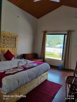 Habitación de hotel con una cama de madera, un almohadón rojo, una ventana con cortinas y vistas al exterior.