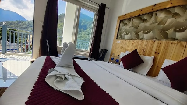 Habitación de hotel con una cama grande, cabecera de madera y vista a las montañas a través de la ventana.