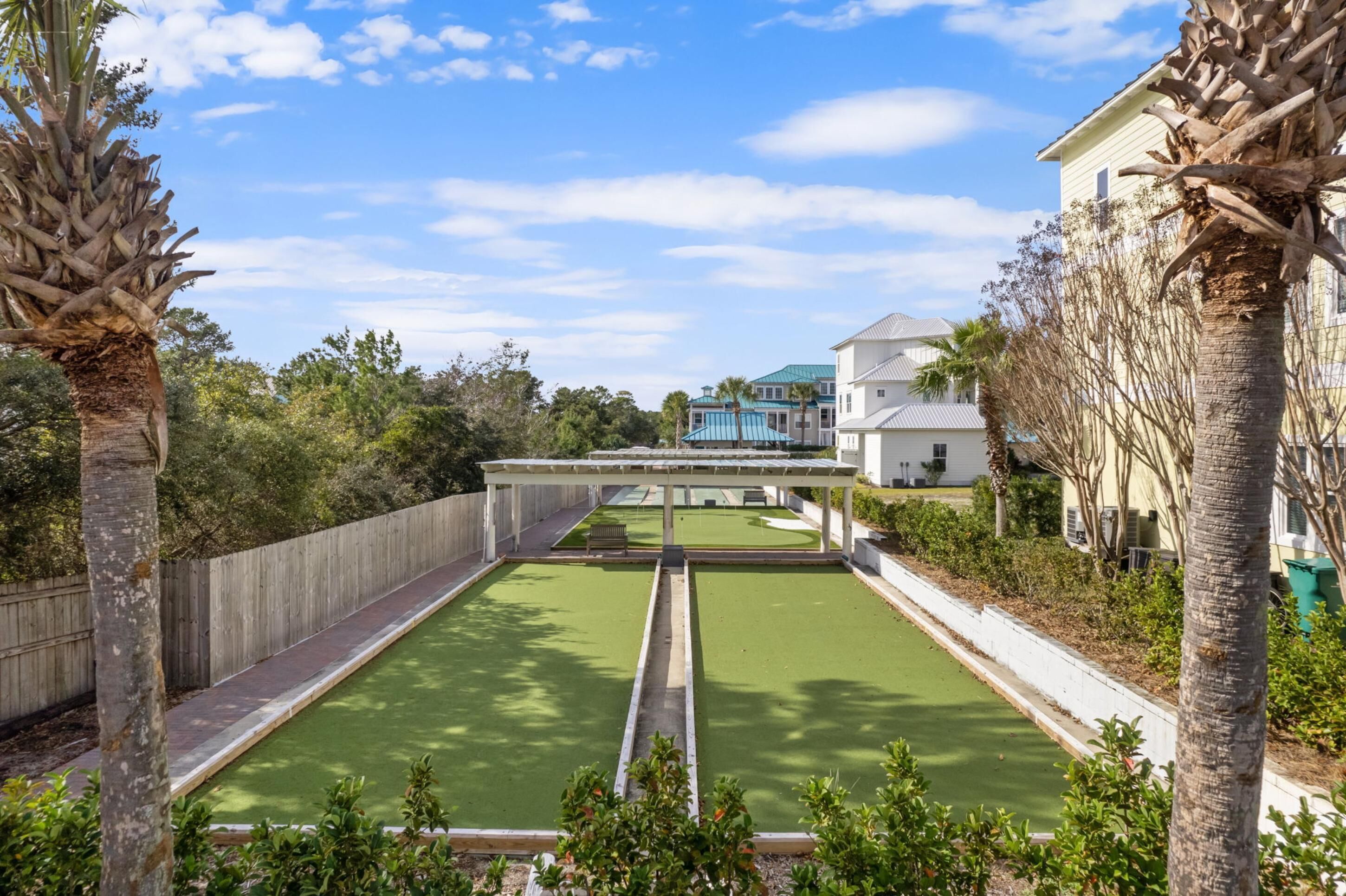 A courtyard with a green lawn, a pergola, and a white fence.