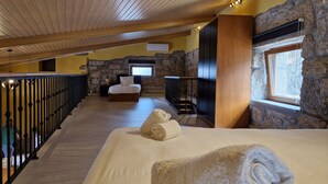 Une chambre d’hôtel avec un plafond en bois, des murs en pierre, un lit avec une literie blanche, une fenêtre donnant sur un paysage agréable et un balcon avec une balustrade.