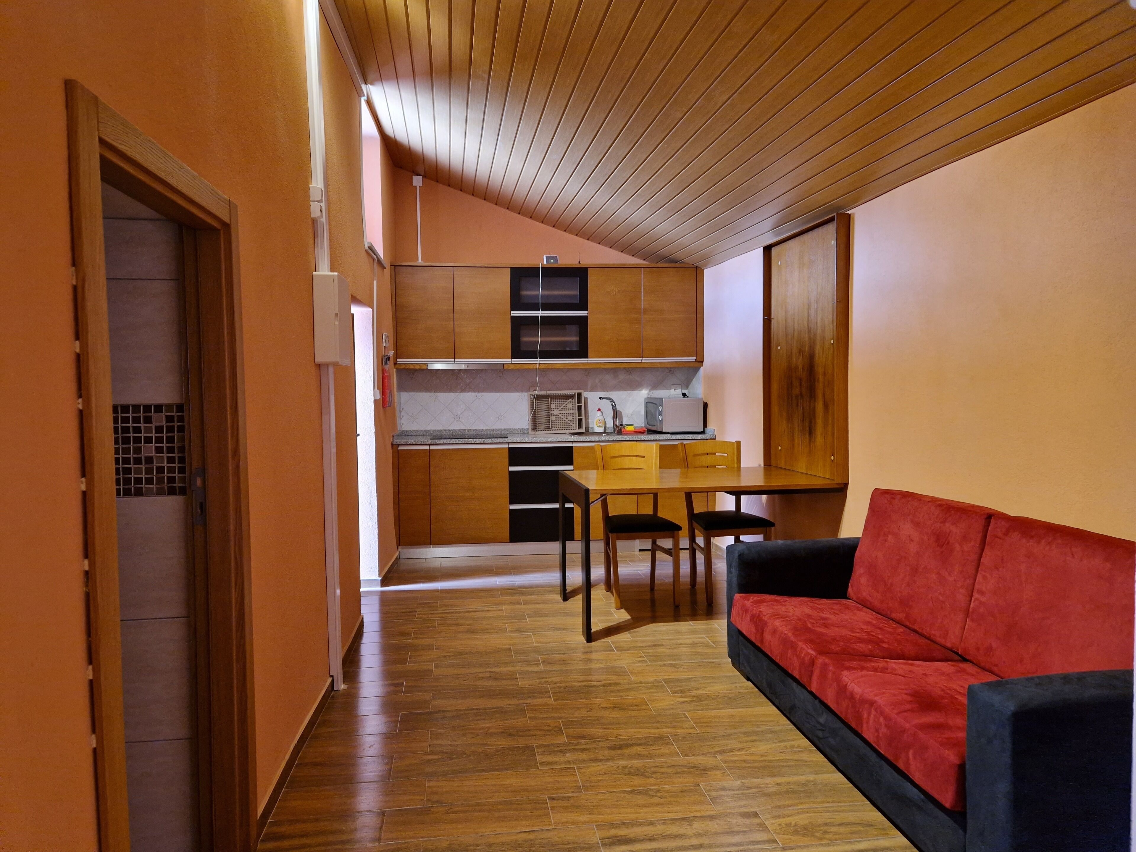 A compact living space with a kitchenette, a dining area, and a red sofa.