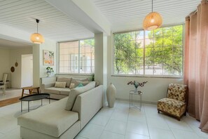 A spacious living room with a sofa, a chair, a table, and a large window with a view of greenery. - Joyful Secret Garden Residence Downtown, House (Chania)