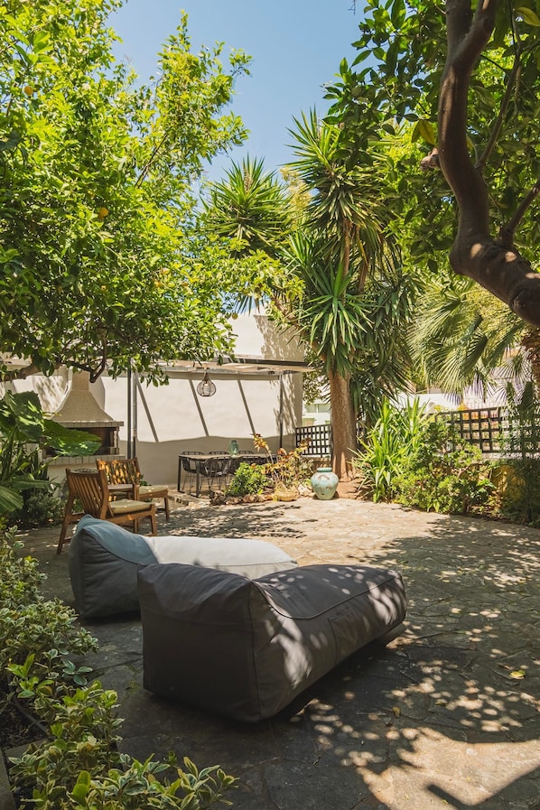 Un patio al aire libre con mesa y sillas, rodeado de abundante follaje y una pérgola.