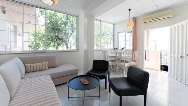 A spacious living area with a sofa, chairs, a coffee table, and large windows offering a view of the outdoors. - Joyful Secret Garden House by 8essentially (Chania)