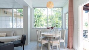 A bright room with a dining table and chairs, a sofa, and large windows with a view of greenery. - Joyful Secret Garden House by 8essentially (Chania)