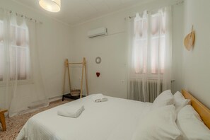 Een hotelkamer met een bed, een houten schommel, een klein mandje, een decoratie in de vorm van een hart en een luchtverkoeler aan de muur.