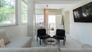 A modern living room with a sofa, two black chairs, a coffee table, and a TV mounted on the wall. - Joyful Secret Garden House by 8essentially (Chania)