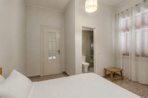 Un dormitorio con cama, puerta, ducha y ventana con cortinas.