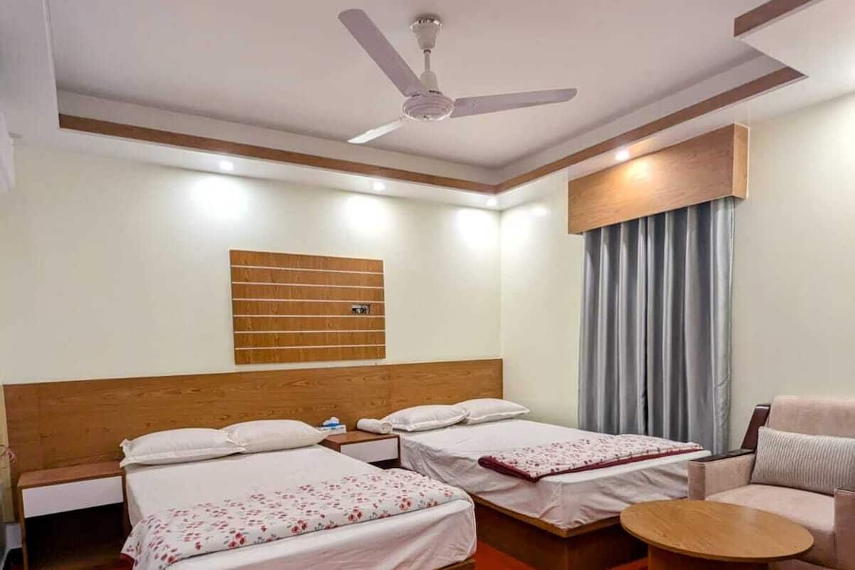 A hotel room with two beds, a wooden headboard, a ceiling fan, a small round table, and a couch.