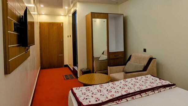 Quarto de hotel com cama, ventoinha no teto, espelho, guarda-roupa e televisão fixada na parede.