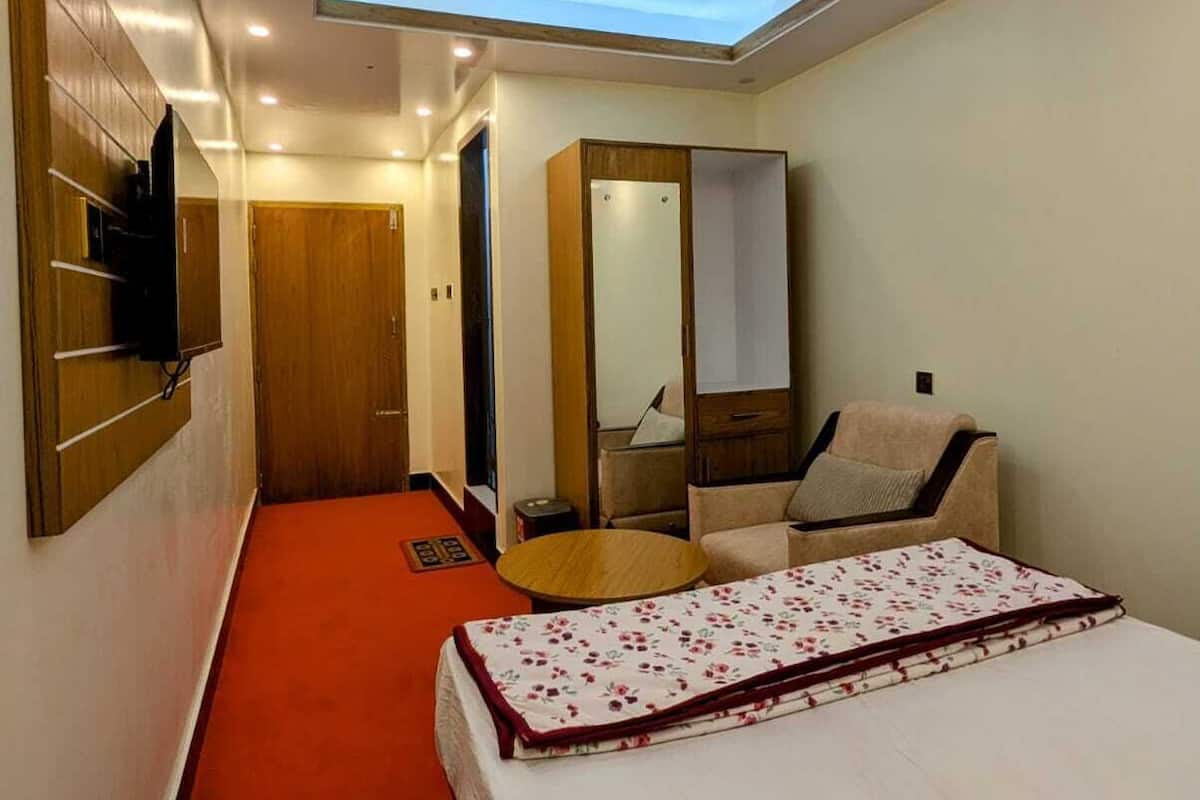 A hotel room with a bed, a ceiling fan, a mirror, a wardrobe, and a TV mounted on the wall.
