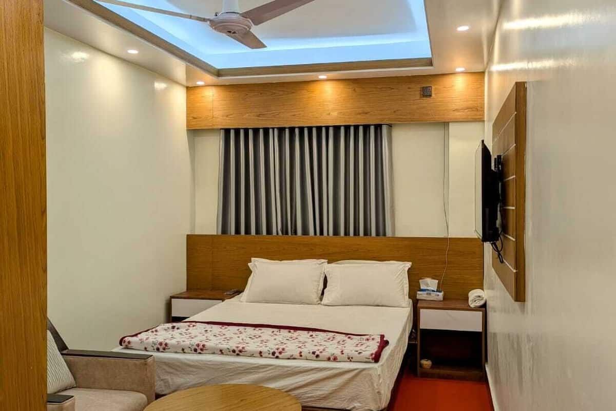 A hotel room with a bed, a small table, a sofa, a ceiling fan, and a TV mounted on the wall.