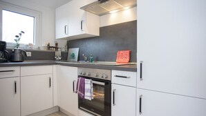 Une cuisine moderne avec des meubles blancs, un four encastré et une fenêtre qui laisse entrer la lumière naturelle.