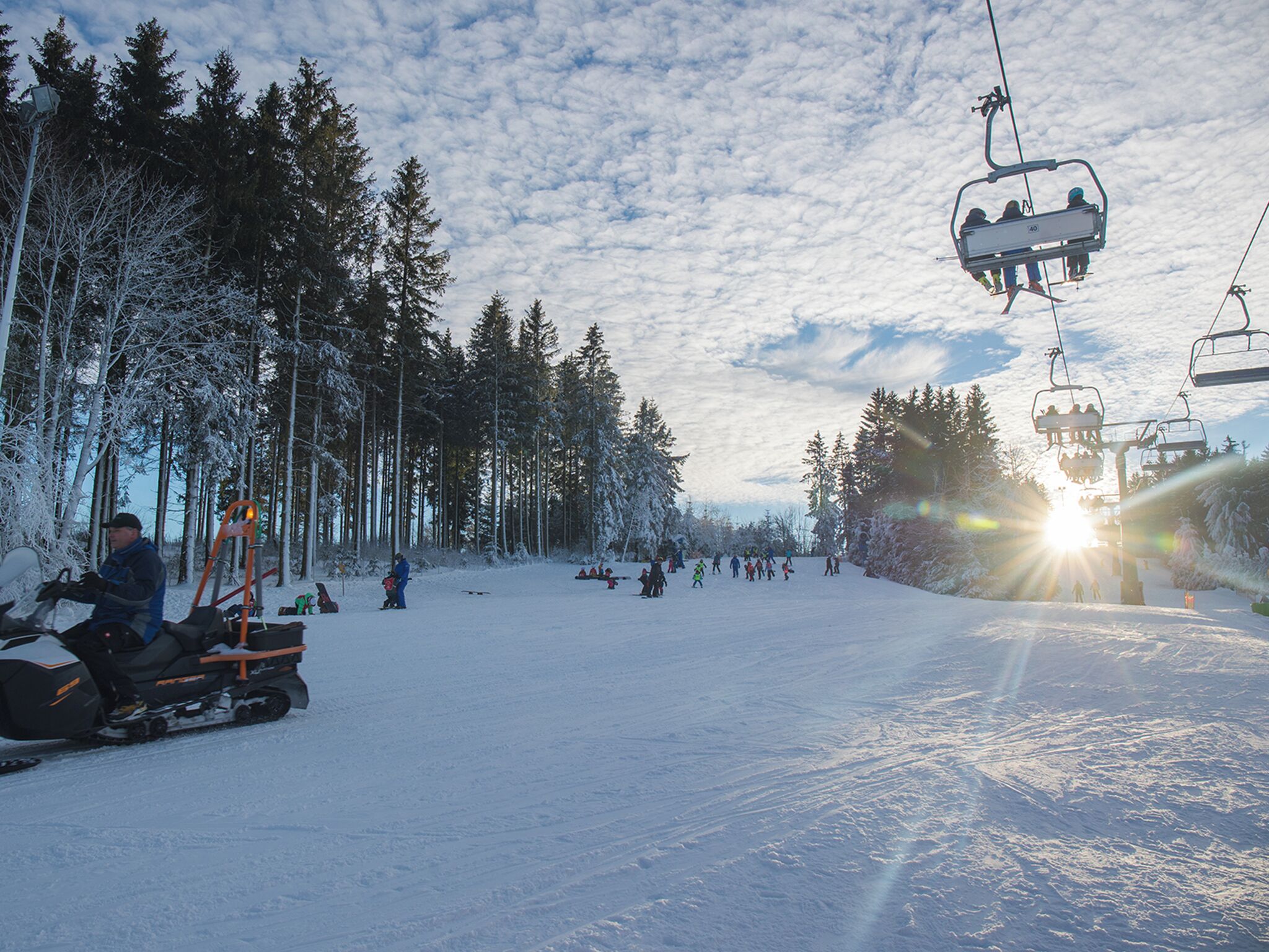 En snötäckt skidbacke med en skidlift och en snöskoter.