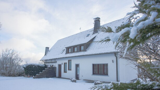 Een huis met twee verdiepingen, een sneeuwbedekte dak en een voortuin.