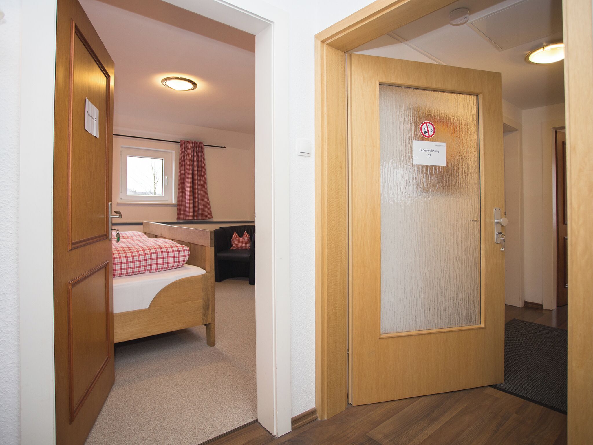A hotel room with a bed, a chair, a window, and a door with a sign.