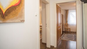 Een gang met een houten vloer, een deur en een vloerkleed dat naar een kamer leidt.