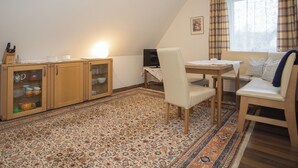 Een gezellige kamer met een eethoek, een bank, een kast met glazen deuren en een kamerbreed tapijt.