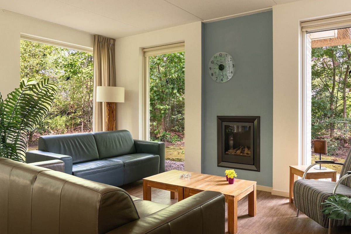 A living room with a sofa, a coffee table, a fireplace, and large windows with a view of greenery.