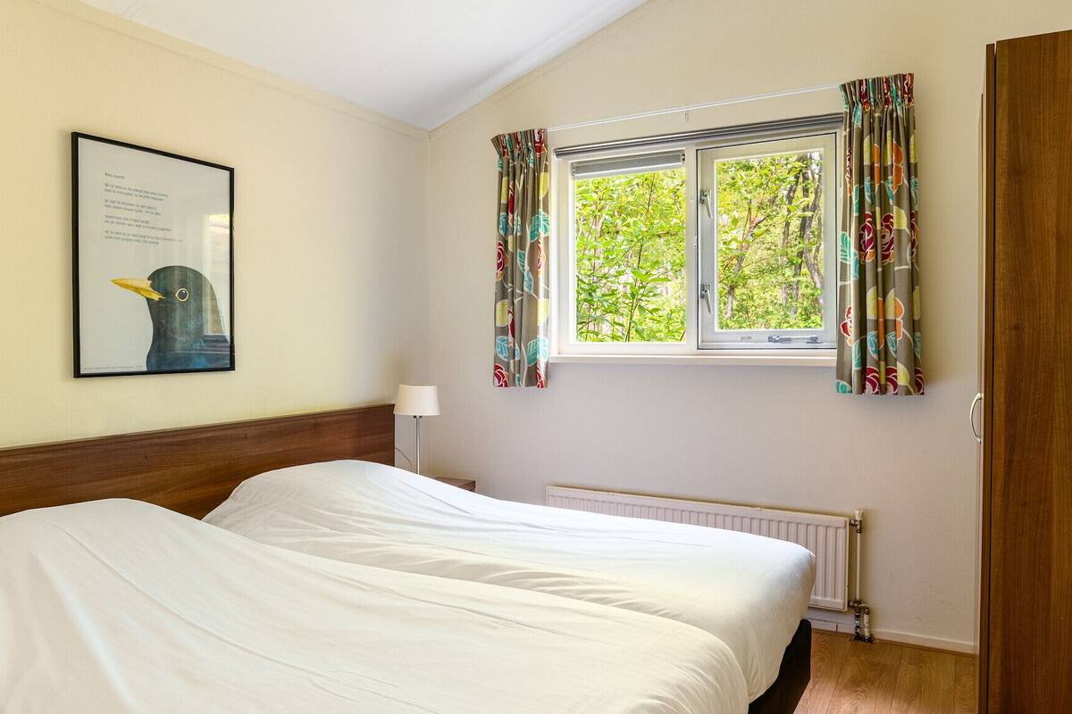 A bedroom with two beds, a window with curtains, a radiator, and a framed picture on the wall.